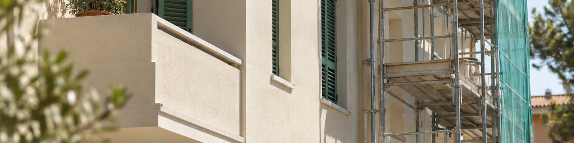 Edificio residenziale in ristrutturazione con facciata chiara, persiane verdi e ponteggio.